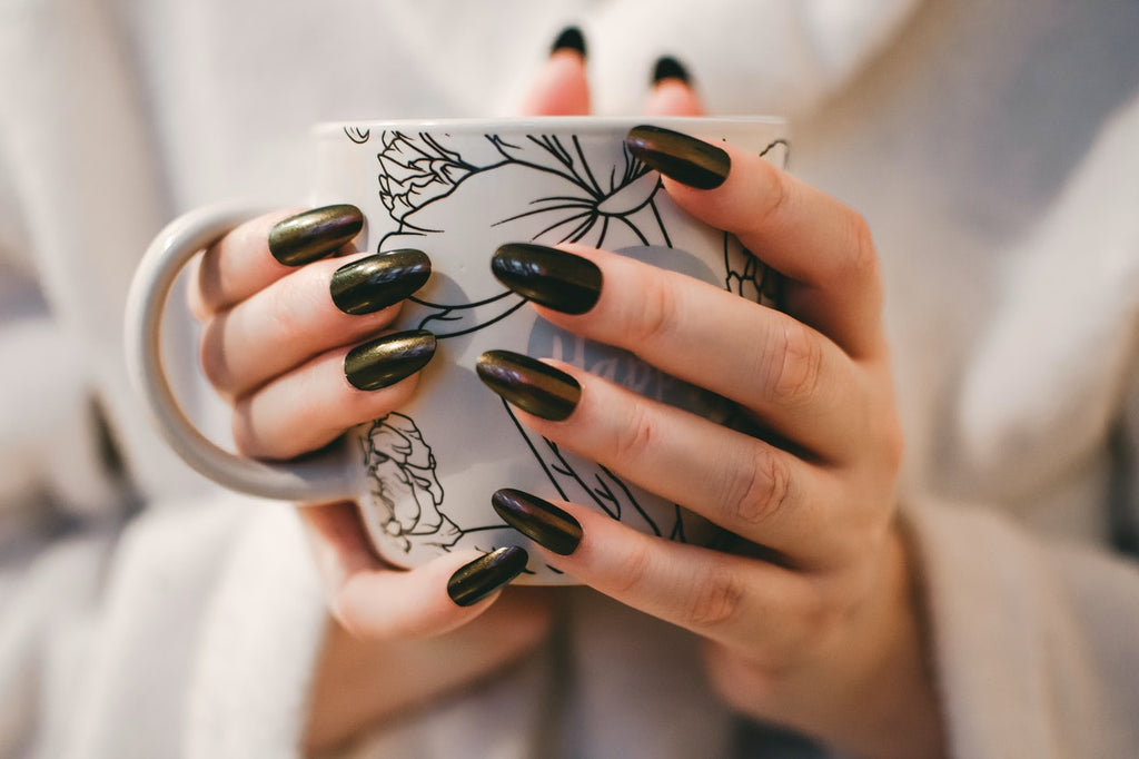 Woman with fake black nails holding a white and gray floral ceramic mug