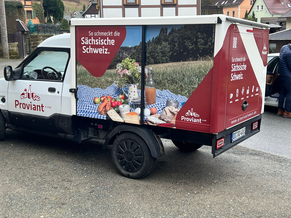 Auf dem Bildzusehen ist ein schön gestalteter E-Transporter, den das Team vom Proviantomatren zum befüllen der Automaten verwendet. Das vollelektrische Fahrzeug ist mit Bildern der Sächsischen Schweiz bedruckt.