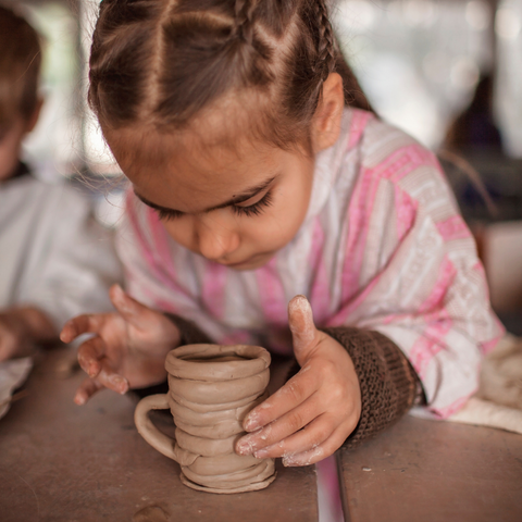 Young girl wearing a pink poncho shaping clay into a cup 