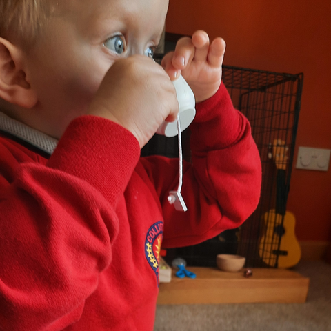 A toddler wearing a red jumper pretending to drink a cup of tea at Messy Makes for Toddlers classes in the Art Attack Angus Studio