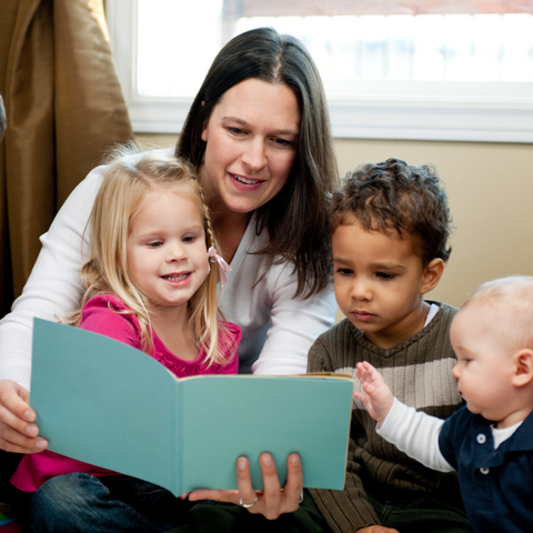 A brunette woman reading a story to three pre-school children