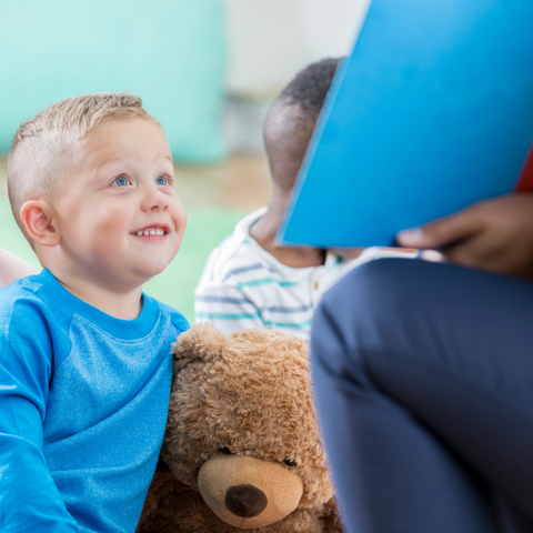 Toddler smiling and listening to a story while cuddling his teddy bear