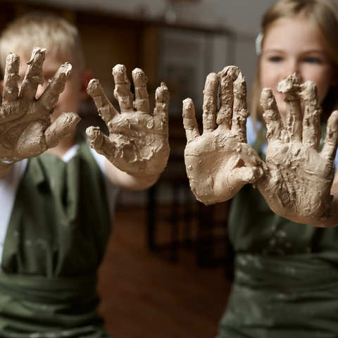 A boy and a girl holding up their hands covered in clay from clay handprint making