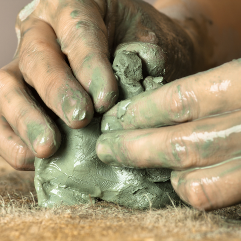 Adult hands shaping wet clay to make a clay handprint