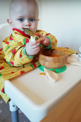 Baby in a highchair with a spoon and a bowl of soup