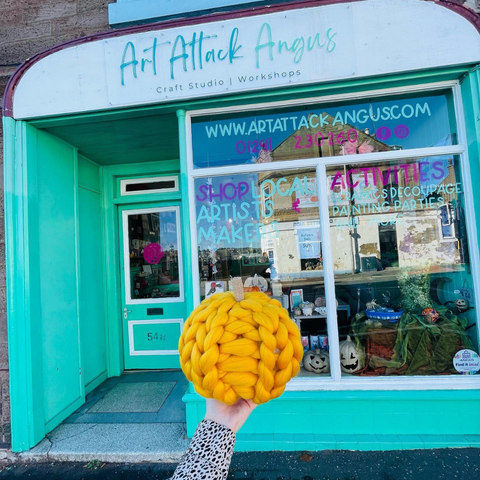 Image shows an orange chunky knit pumpkin being held up in front of the Art Attack Angus store front