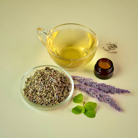 loose leaf lemon balm and lavender tea with a cup of brewed herbal tea, fresh lavender and fresh mint and a soothing foot massage balm on a light green background