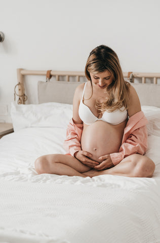 Pregnant woman sitting on a bed looking at her bump while holding it