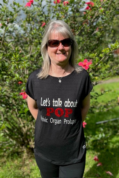 Bronwyn Ford wears a shirt that says "Let's talk about Pelvic Organ Prolapse" in front of flowers