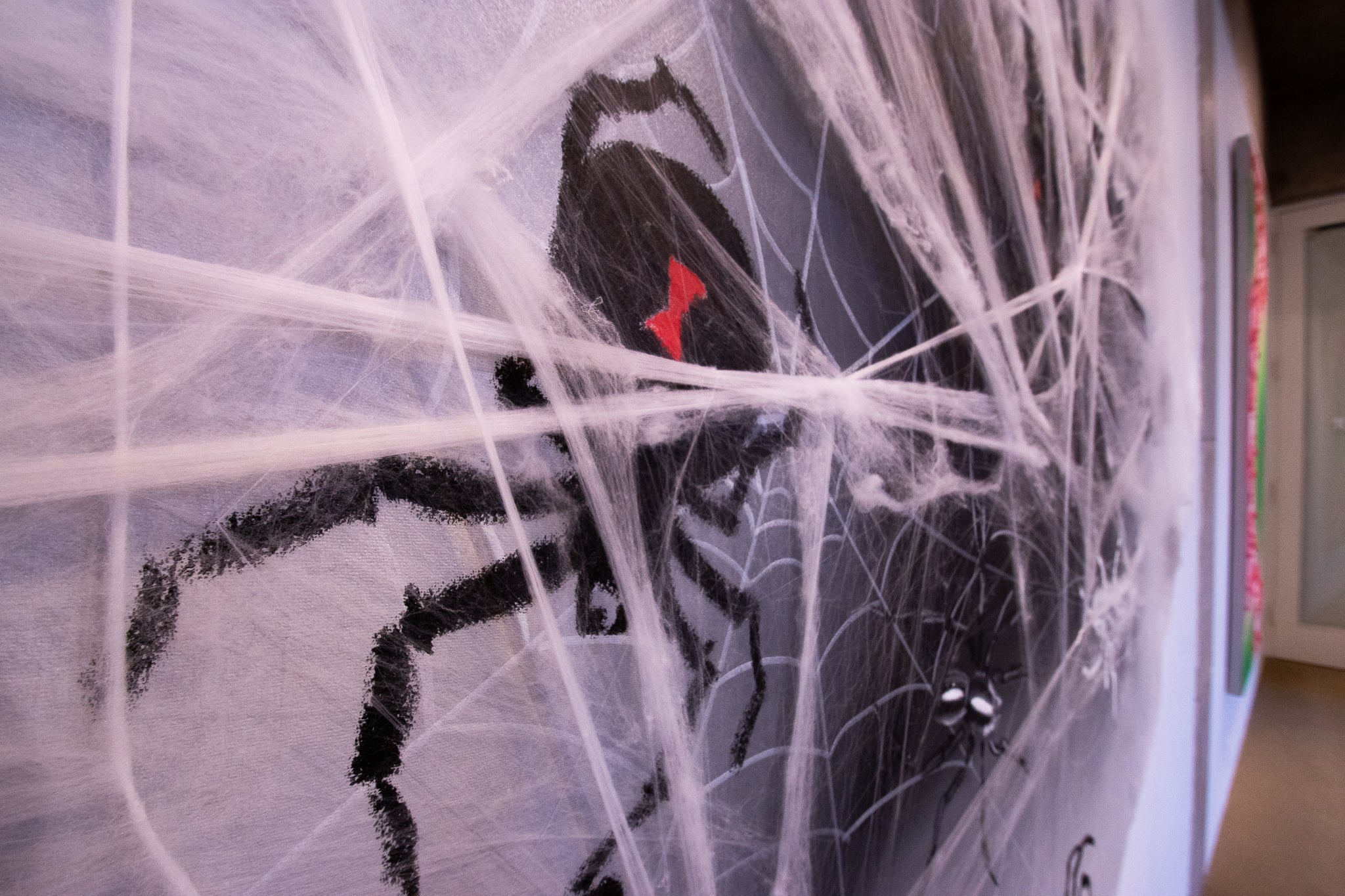 Cotton spiderwebs stretch over an oil stick drawing of a black widow spider. The web sticks out the canvas just enough to provide texture, but when seen from the front, looks almost like it was drawn onto the painting.