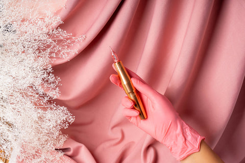 Rose gold PMU machine in artist's hand over top pink drapery