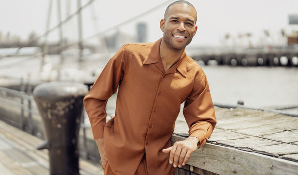 a man leaning on a wooden pier fence. he is wearing a tan walking suit.