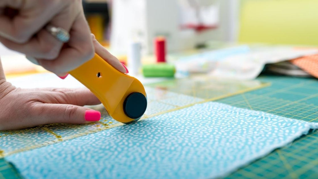 A person using a roller cutter to cut a piece of fabric. 