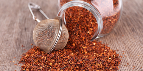 Rooibos loose leaf tea spilling out of a jar with a tea infuser in the foreground