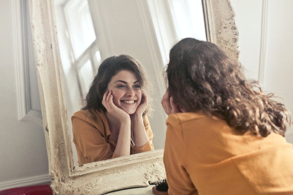 Woman Looking in mirror giving herself positive self talk and affirmations