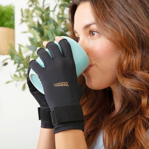 Woman enjoying a hot beverage while wearing her Hand Relief Compression Gloves.