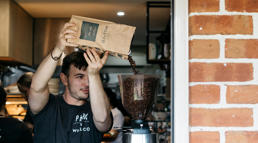 A barista pouring beans into the machine's hopper