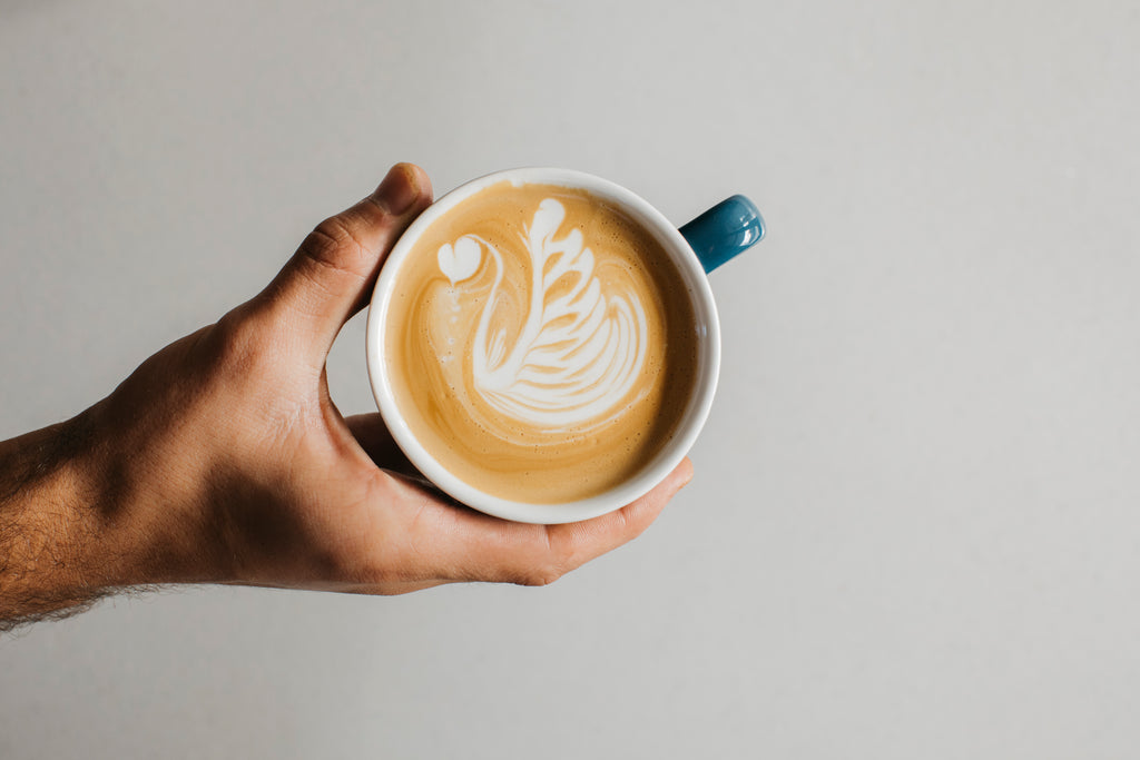 A close up of a barista's hand holding a cup of freshly made coffee