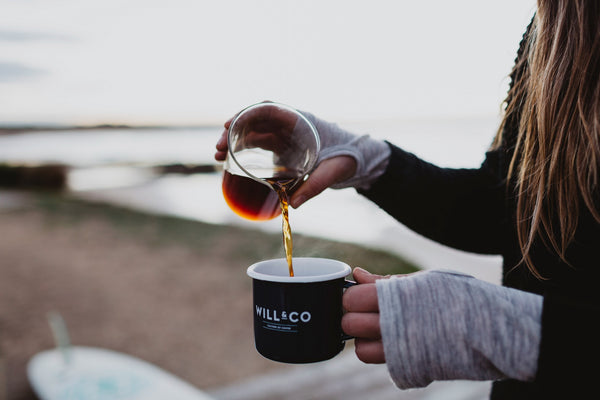 A young woman pouring black coffee into a Will & Co branded mug