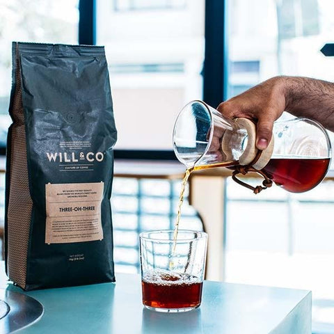 A bag of Will & Co Three-oh-Three specialty beans and a black coffee being poured into a glass