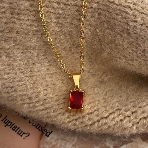 A close-up photo of a dainty 18k gold pendant necklace on a white background, the pendant is round in shape with a small diamond in the center and hanging on a thin gold chain