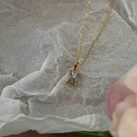 A close-up photo of a dainty 18k gold pendant necklace on a white background, the pendant is round in shape with a small diamond in the center and hanging on a thin gold chain