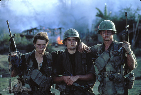 Platoon movie image with William Hurt, Charlie Sheen, and Tom Beringer standing in a field in Vietnam with burning trees and smoke in the background