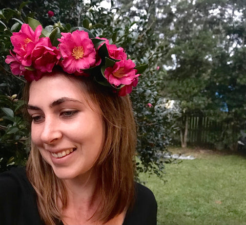 Woman smiling and wearing a flower crown in front of a bush and garden.