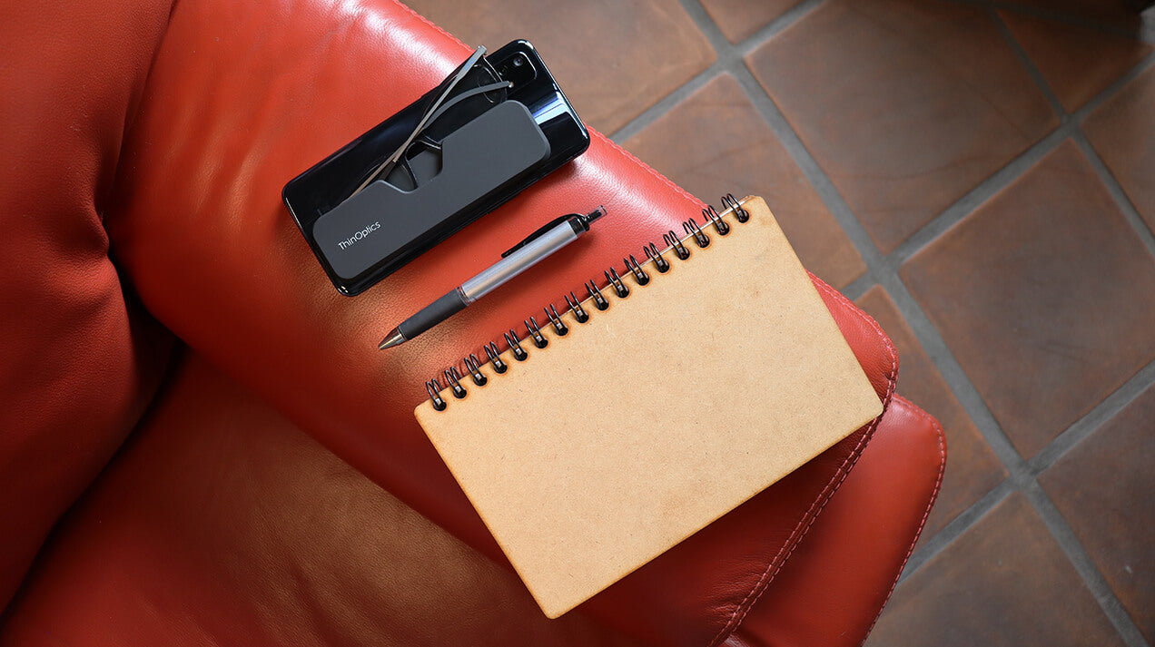 A pair of Connect Reading Glasses in a Connect Case attached to the back of a phone