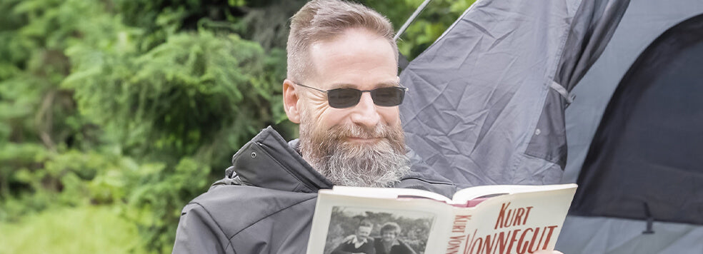 Man wearing Brooklyn Reading Sunglasses while reading a book in front of a camping tent