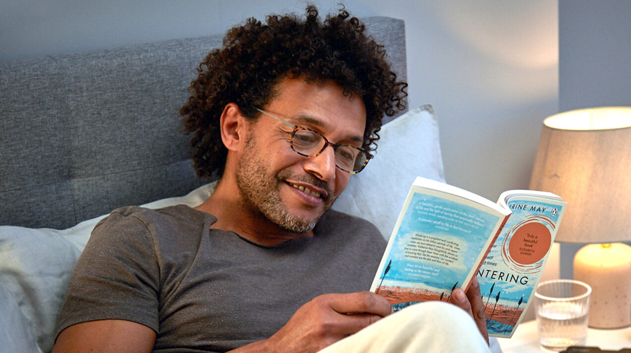Man sitting in bed reading a book while wearing Reading Glasses