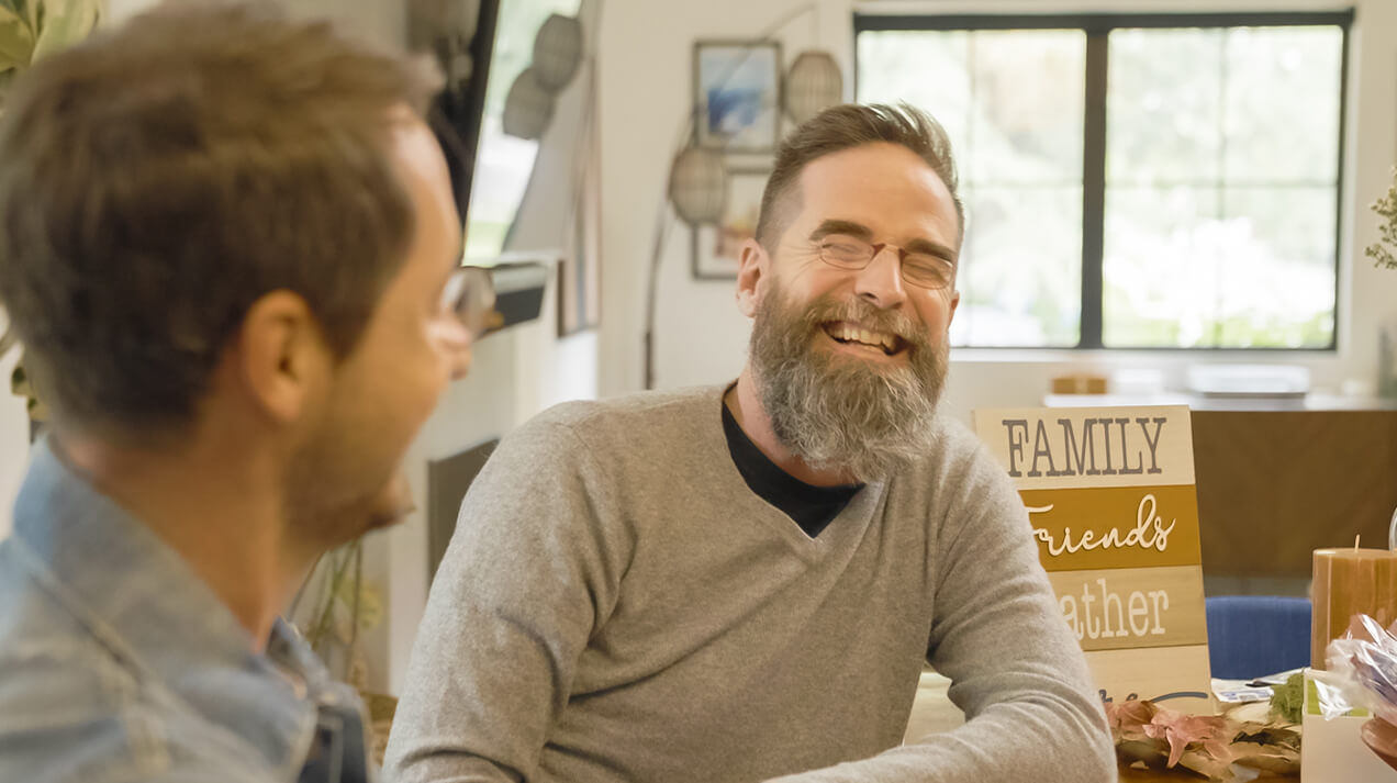 Two men sitting at a table conversing, one is wearing Readers and the other is wearing a pair of Manhattan Reading Glasses