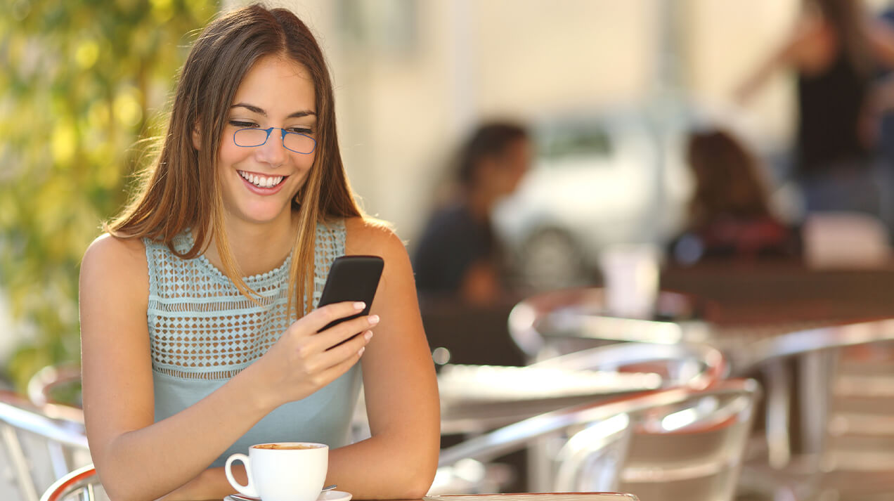 Woman wearing Readers while looking at her phone as she sits in a cafe