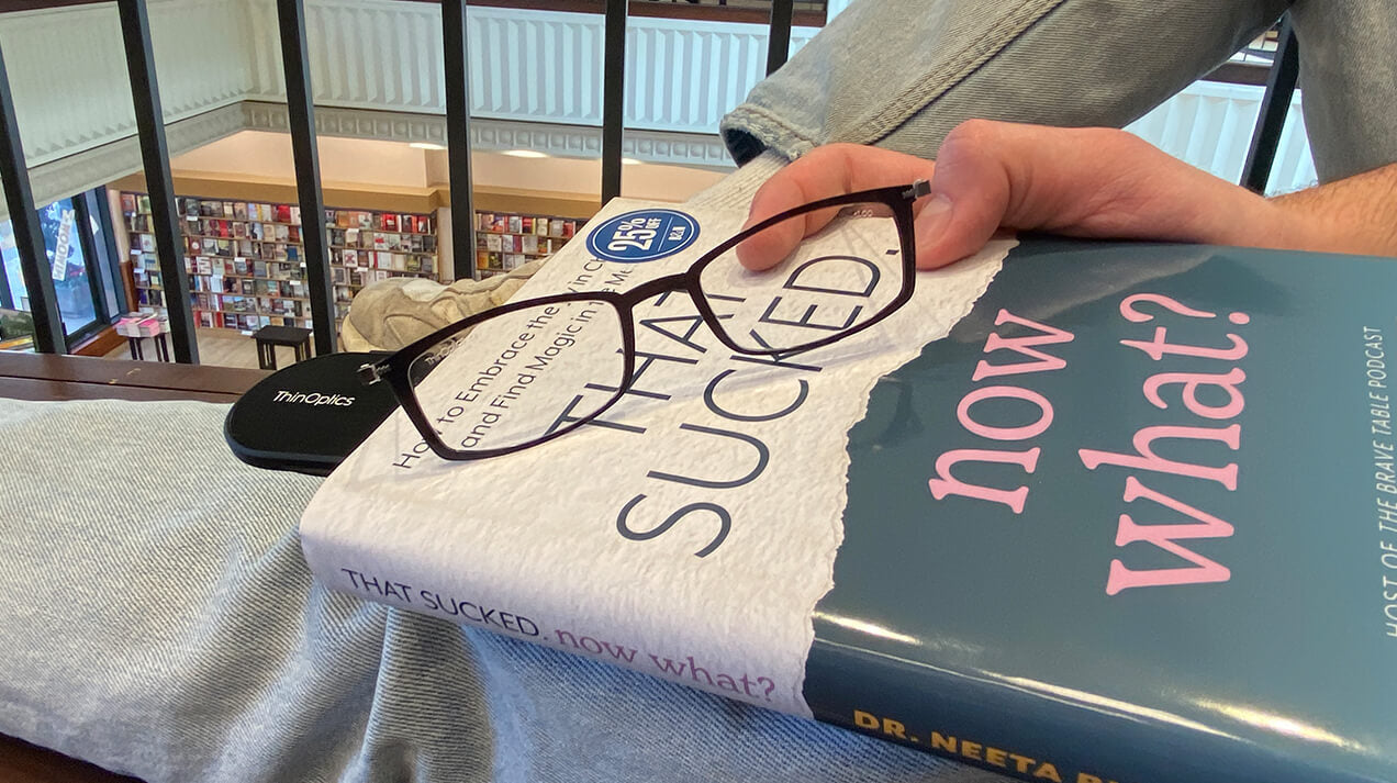 Two men sitting at a table conversing, one is wearing Readers and the other is wearing a pair of Manhattan Reading Glasses