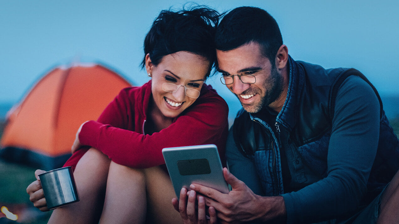 Man and woman wearing Readers while camping outdoors and looking at their tablet