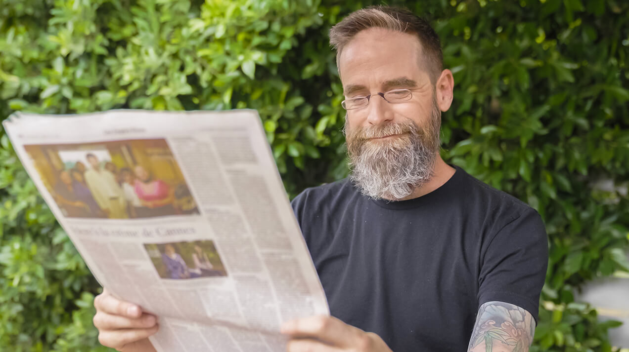 Man reading newspapers outdoors while wearing Headline Readers