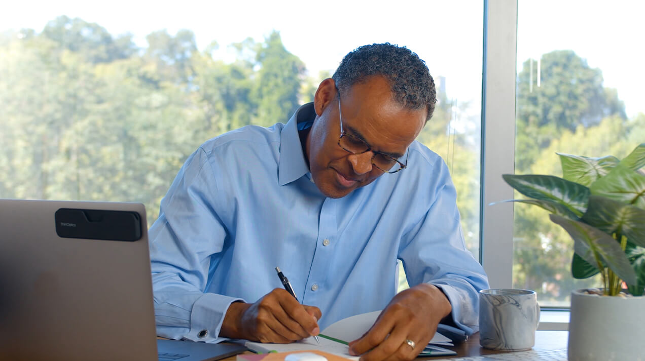 Man working at his desk wearing the Connect Reading Glasses and has the Connect Case attached to the back of his laptop.