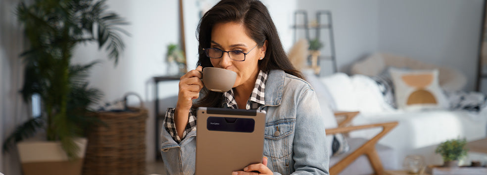 Woman wearing Brooklyn Reading Glasses while drinking coffee and looking at her tablet with a Connect Case attached to the back