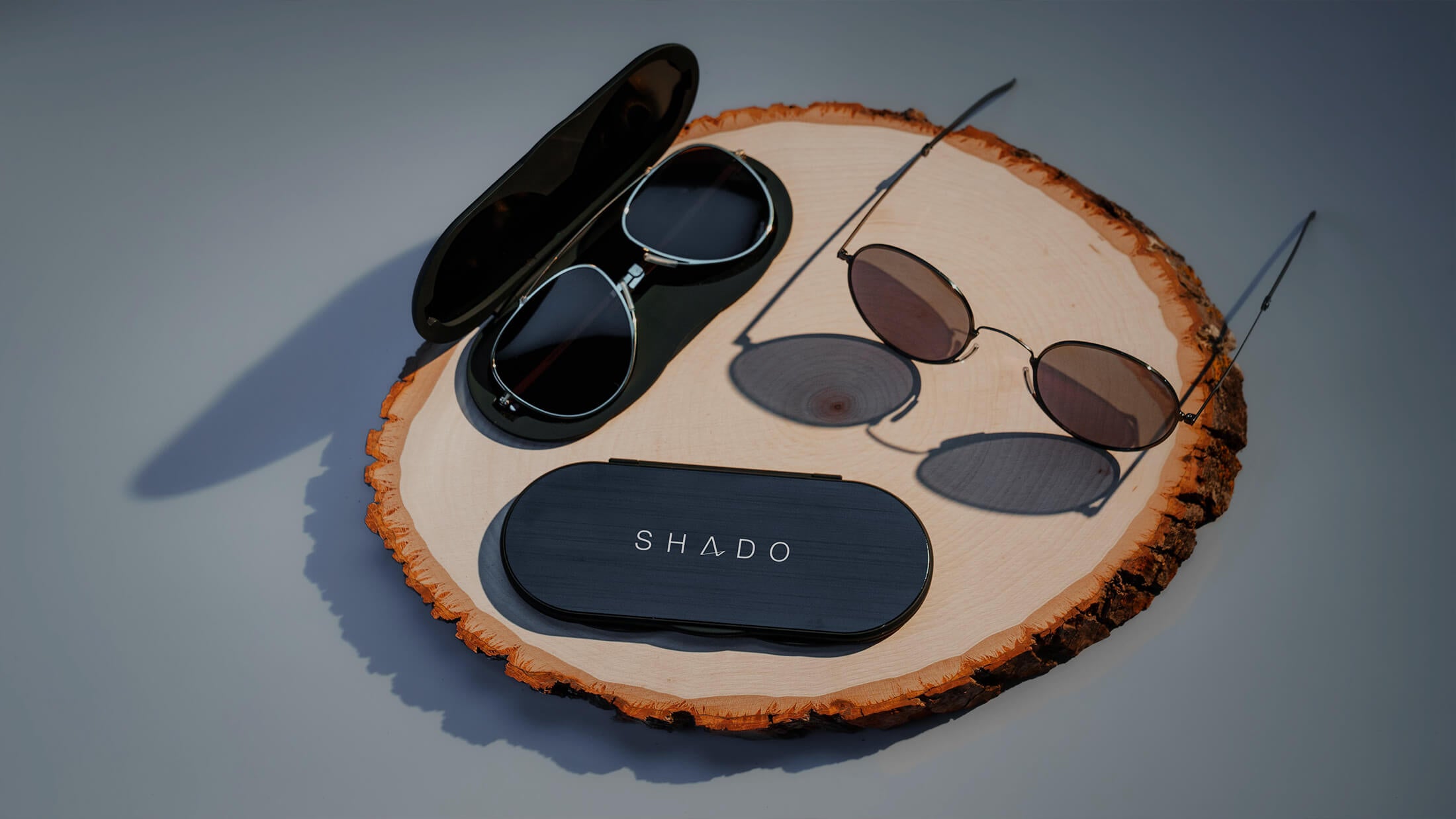 Two pairs of sunglasses and a case on a wood block