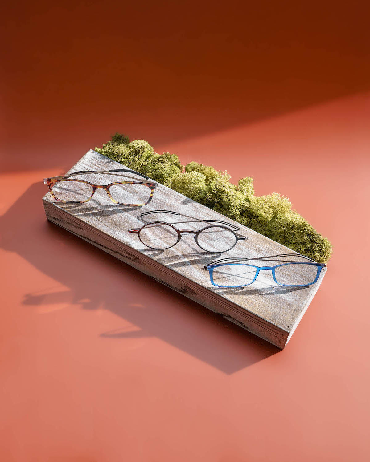 Elegant selection of ThinOptics reading glasses in various frame shapes and vibrant colors, presented on a rustic wooden plank against a warm orange backdrop, highlighting the stylish versatility and color options available.