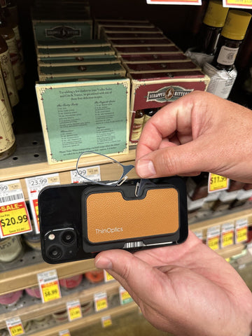 Close-up of a hand pulling out ThinOptics Reading Glasses from the Universal Pod Wallet attached to the back of a phone with MagSafe® technology.