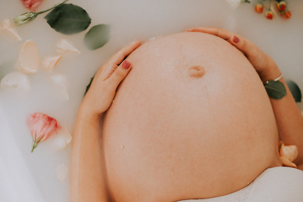 pregnant woman sitting in bath tub with flower petals.