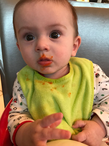 Baby with green bib and pureed bananas on his face