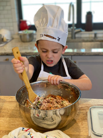 Small boy cooking in the kitchen mixing a bowl of meatballs with a chef hat on