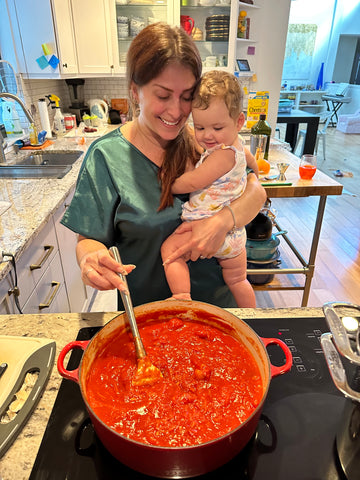 Mom in green dressing cooking marinara sauce in her kitchen with her baby