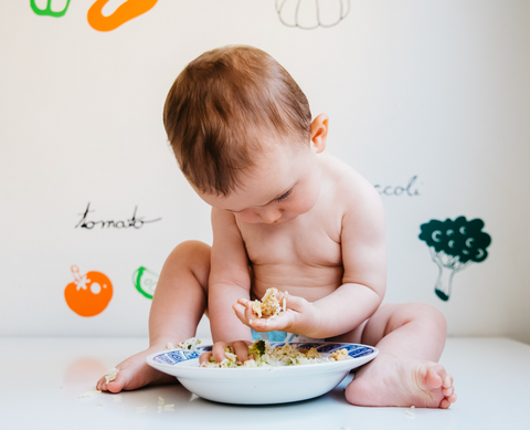 Baby with diaper on explores bowl full of salad