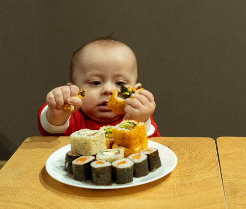 Baby eating a big plate of different sushi rolls