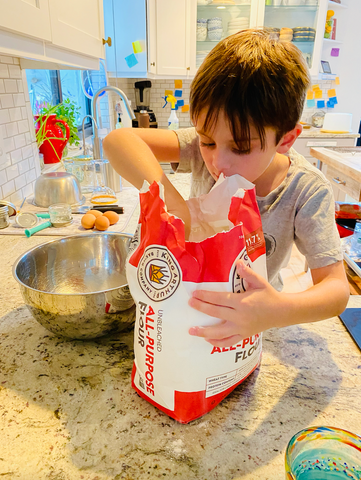 Little boy scooping flour into a mixing bowl
