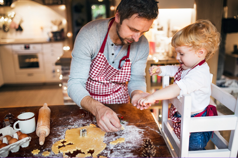 Dad in red and white apron baking holiday cookies with toddler child