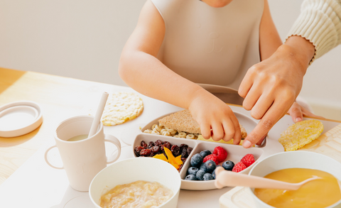 Small child eating a plate of fruits, vegetables and whole grains